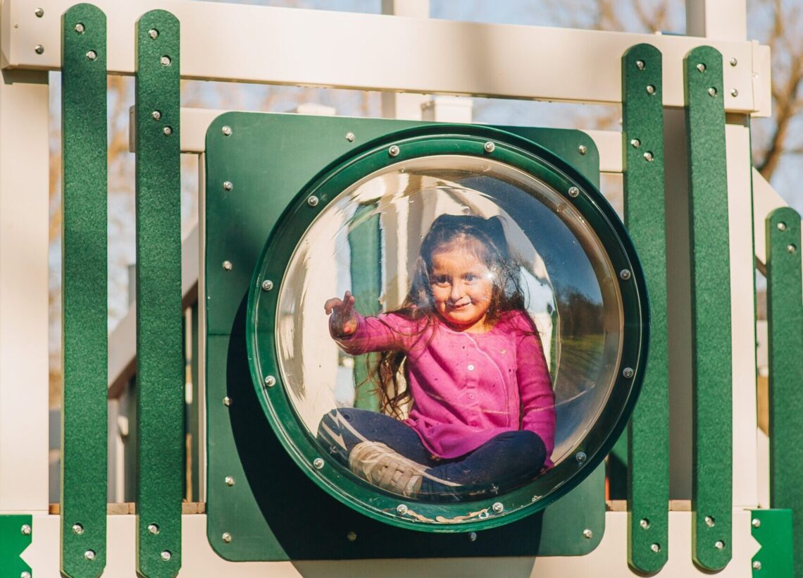 A little girl is peering through a bubble panel on a King Swings Commercial playground.