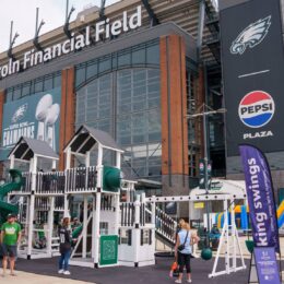 Exterior of Lincoln Financial Field with large sign and Eagles banners; people at a fan event outside the stadium.