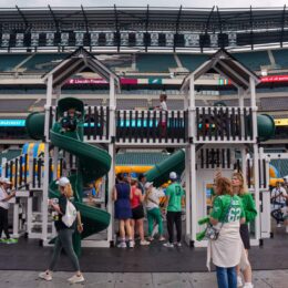 Family-friendly event in a stadium with a large playground structure and slides, people walking and talking around the area.