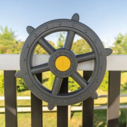 A gray ship's wheel on a playground.